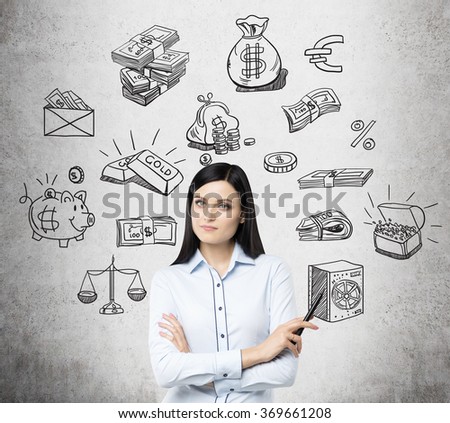 beautiful woman pointing at a picture of a safe, other black pictures symbolizing money around her. Concrete background. Front view. Concept of running into money.