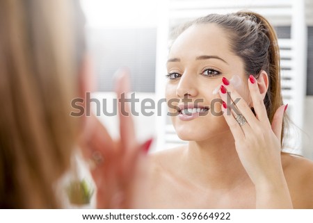 Attractive girl putting anti-aging cream on her face Royalty-Free Stock Photo #369664922