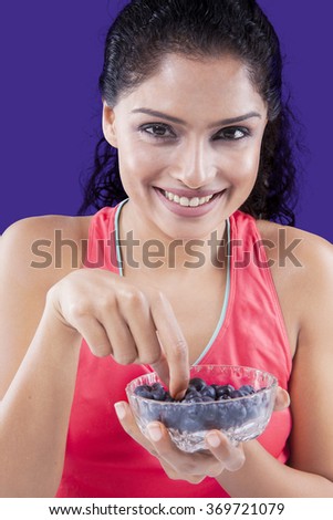 Picture of indian young woman holding a bowl of blueberries while smiling at the camera
