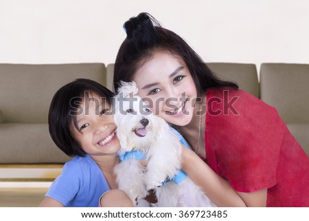 Picture of young woman and her daughter smiling at the camera while hugging a maltese dog at home