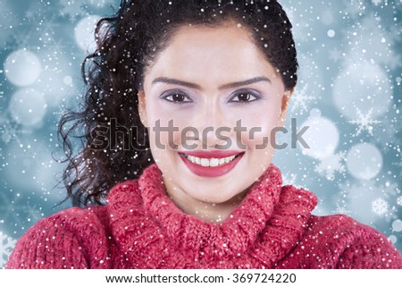 Picture of attractive indian woman smiling at the camera while wearing warm clothes with winter background