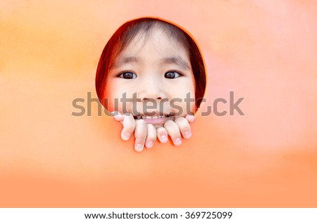 cute asian girl looking out of plastic hole outdoor play park