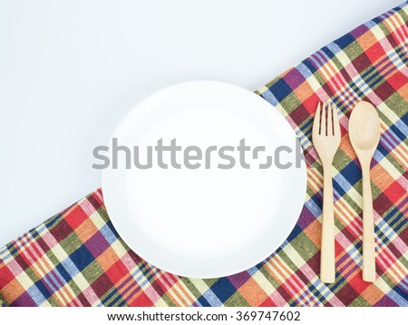 White dish with wooden spoon and fork on colorful tablecloth.