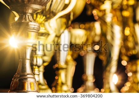 Group of the golden trophies in sparkling light on the dark background. Royalty-Free Stock Photo #369804200