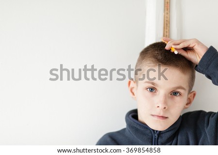 Handsome Boy Standing on the Wall with Measuring Stick to Check his Height While Looking Straight at the Camera. Emphasizing Copy Space on the Left Side. Royalty-Free Stock Photo #369854858