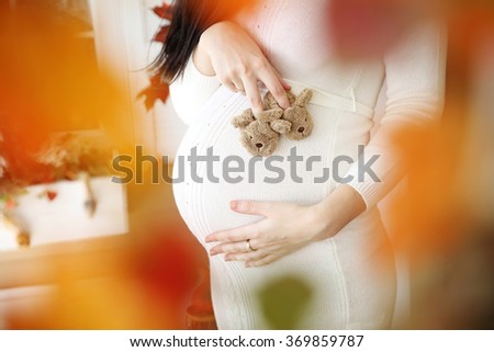 Pregnant belly in white dress with small rabbit slippers on it