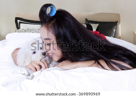 Picture of young woman with long hair lying on the bedroom while hugging her dog