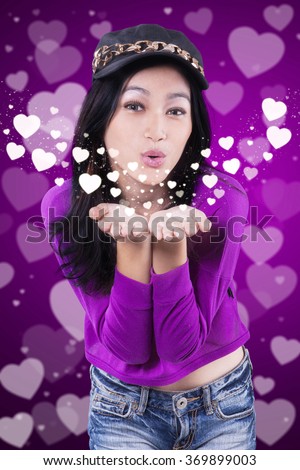 Portrait of beautiful teenage girl blowing kiss at the camera with purple background
