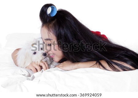 Picture of cheerful pretty woman with long hair smiling happy while hugging a maltese dog on the bed