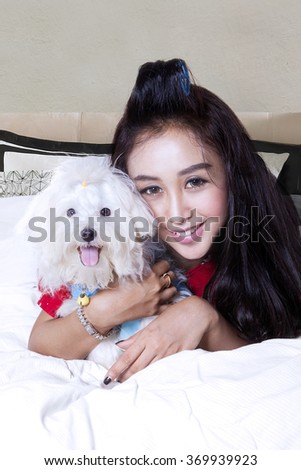 Picture of beautiful young woman embracing a maltese dog on the bed and smiling at the camera