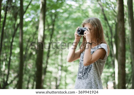 Young girl in casual clothes with old retro vintage camera photographing in forest. Brown hair, long legs, slim body.