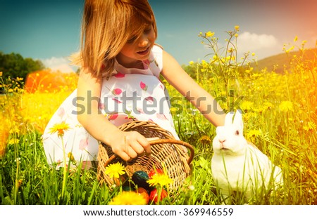 Girl petting Easter bunny on meadow with eggs - filtered image
