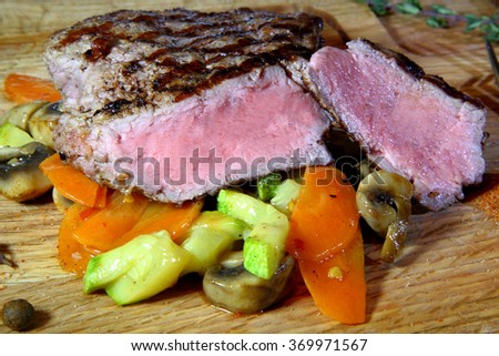 Juicy Grilled Steak. Beef steak medium rare on vegetable cushion. Beef steak on wooden plate plate - Stock Image
