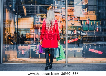 Woman looking at window shop - Young pretty girl standing in front of a boutique holding shopping paperbags Royalty-Free Stock Photo #369974669