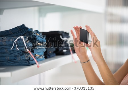 Cropped image of woman photographing jeans through smartphone in retail store