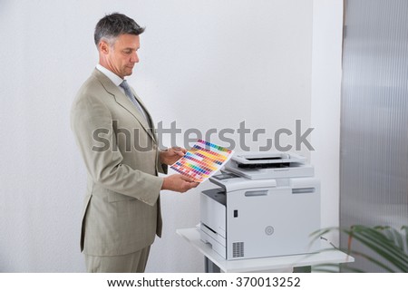 Side view of businessman looking at multi colored paper by color printer in office
