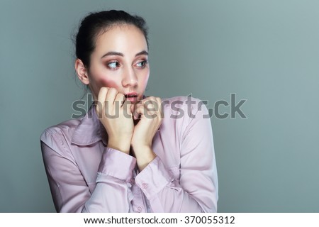 Closeup portrait headshot young unsure hesitant nervous woman biting her fingernails craving for something or anxious, isolated grey wall background. Negative human emotions facial expression feeling  Royalty-Free Stock Photo #370055312