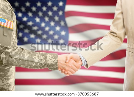 American soldier in uniform and civil man in suit shaking hands with national flag on background - United States