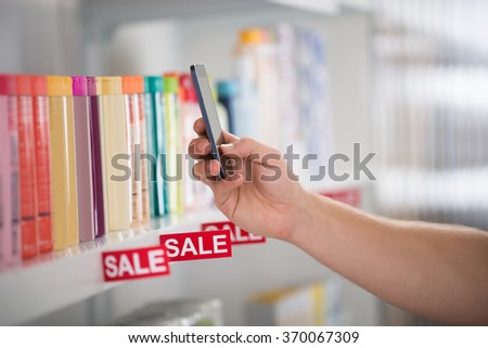 Closeup photo of customer photographing cosmetic product arranged on shelf in supermarket