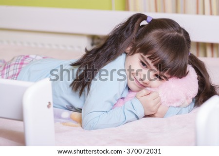 Adorable little girl hugging her teddy bear in bed. Image with shallow depth of field