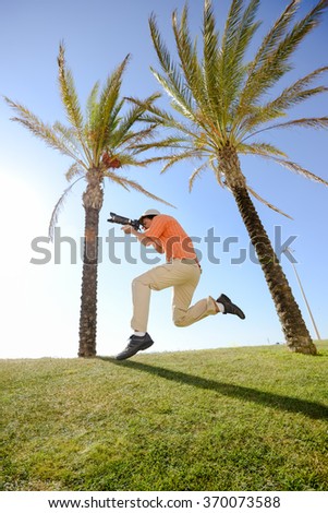 Funny photographer joyful jumping on the palm, green grass and blue sky background