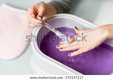 Female hands taking procedure in a lilac paraffin wax  bowl. Cosmetology and skincare equipment in a beauty & spa salon. Royalty-Free Stock Photo #370147217