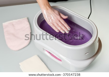 Female hands taking procedure in a lilac paraffin wax  bowl. Cosmetology and skincare equipment in a beauty & spa salon. Royalty-Free Stock Photo #370147238
