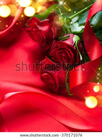 Valentine gift background. Valentine's Day Red Roses bouquet over silk background. Wedding or Valentines Gift. Art design with bunch of beautiful flowers and red satin ribbon closeup