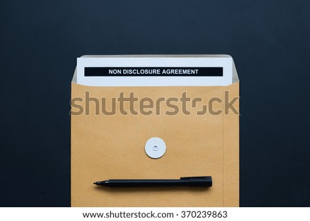 "Non Disclosure Agreement" paper in brown envelope with black pen on black color background.