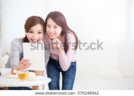 Two happy young female friends use digital tablet pc with tea, coffee and cakes, healthy lifestyle and tecnology concept, asian beauty