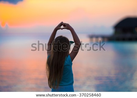 Silhouette of little girl making heart at sunset on the beach