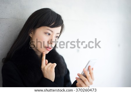 beautiful young woman in black coat holding smart phone