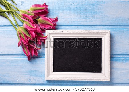 Pink  tulips and  empty blackboard for text  on blue  painted wooden background. Selective focus. Place for text.