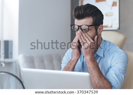 Feeling tired. Frustrated young handsome man looking exhausted and covering his face with hands while sitting at his working place  Royalty-Free Stock Photo #370347539