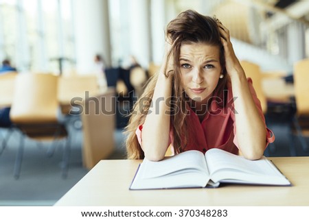Female student studying and reading in a library but is having a hard time understanding the material