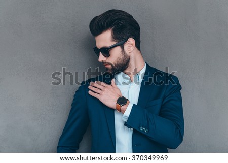 Shake it off. Close-up of young handsome man in sunglasses shaking off invisible dust from his shoulder while standing against grey background Royalty-Free Stock Photo #370349969