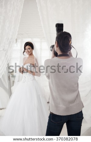 Beautiful bride posing in white room front of female photographer.
