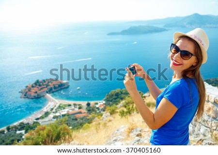 Girl in the hat making photos by the smartphone near the island of Sveti Stefan, Montenegro, Balkans