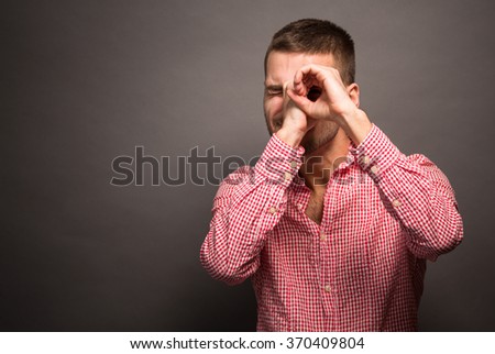 Handsome young man smiling and making binocular or tube with his hands isolated over grey background.