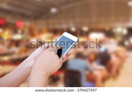 hand hold and touch screen smart phone, on blurred photo of people in food center with light bokeh