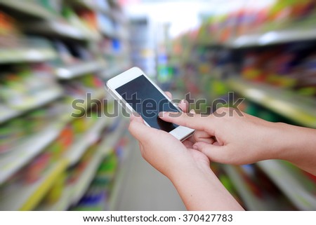 hand hold and touch screen smart phone, on blurred photo of minimart convenience store