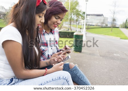 Two smiling woman friends sharing social media in a smart phone in the park.