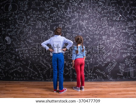 Cute little boy and girl in front of a big blackboard.
