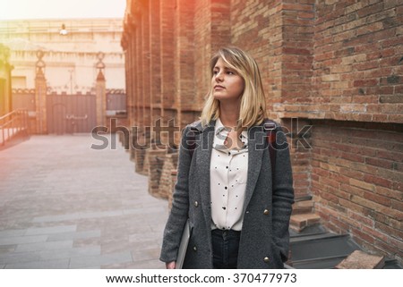 portrait of young beautiful woman with blonde hair wearing a gray coat posing on a background of red brick wall with copy space area for your text or design.flare light
