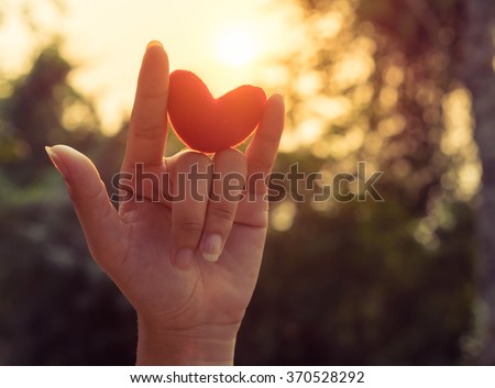Love hand sign with red heart up to the sunset light and flare