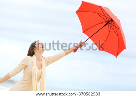 Playful girl joking with a red umbrella on the beach with the sky in the background