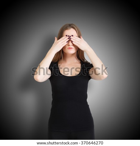 Young woman in black clothes isolated at black background showing blind - hides her eyes with hands, closes them. Concept of indifference.