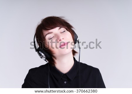 brunette business woman listening to music on headphones, black shirt, studio isolated on grey background portrait emotions