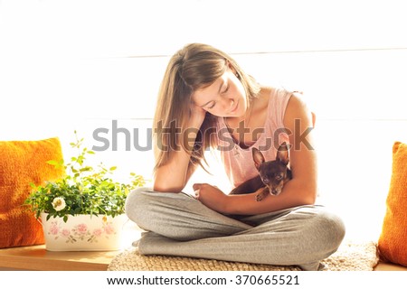 Good morning! Young girl in pyjamas holding her lovely Toy-terrier dog in rays of sunlight. Multicolored vibrant horizontal indoors image with filter.