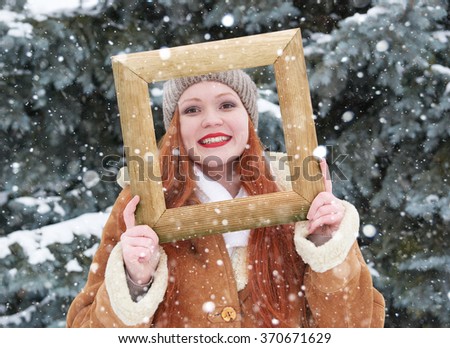 Woman outdoor portrait in wooden photo frame at winter season. Snowy weather in fir tree forest.